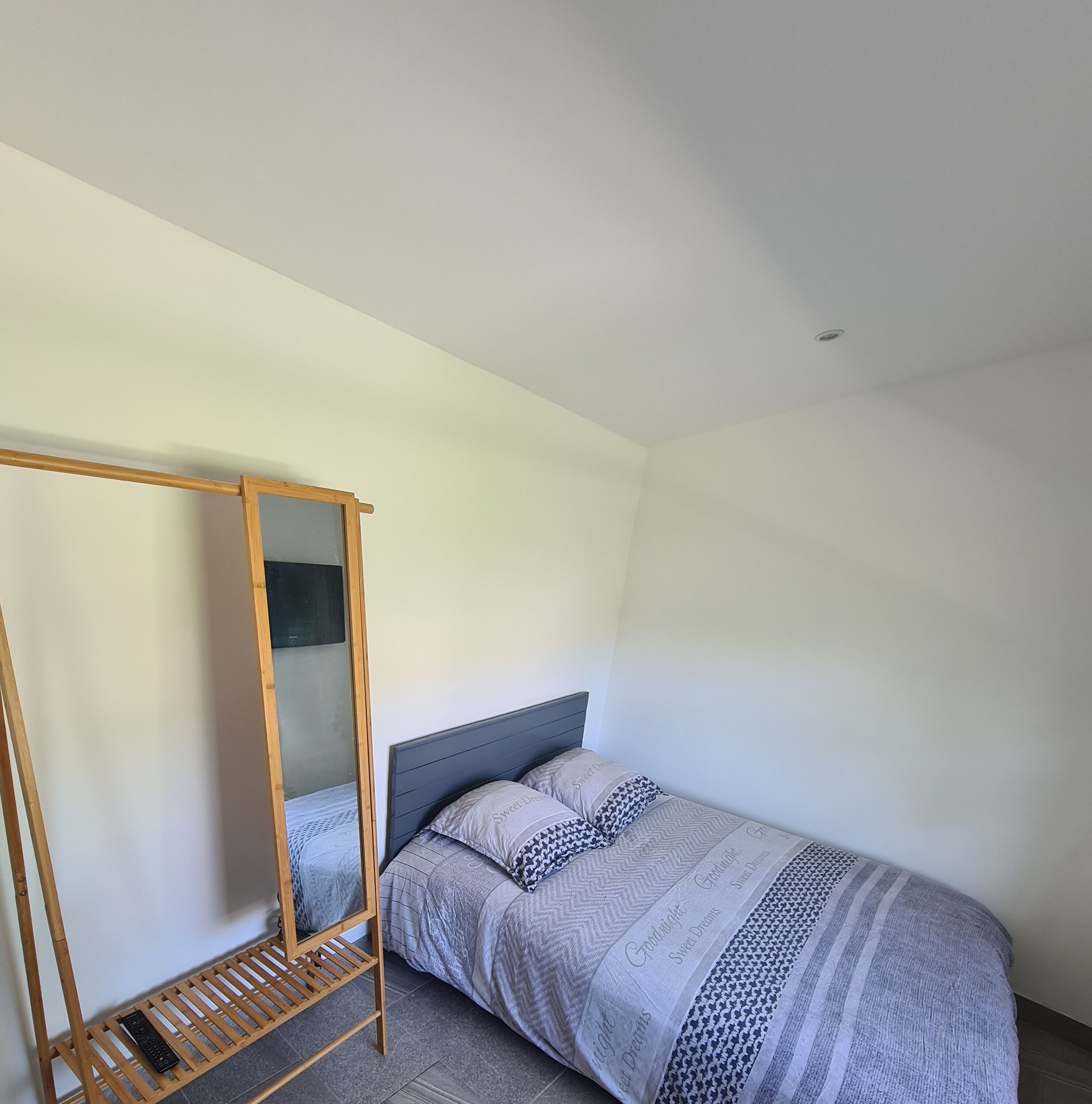 Un dormitorio con una cama individual, una escalera de madera y un pequeño estante con un mando a distancia.