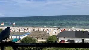 Vista costera con playa, un edificio de techo de paja y una estructura con bandera.