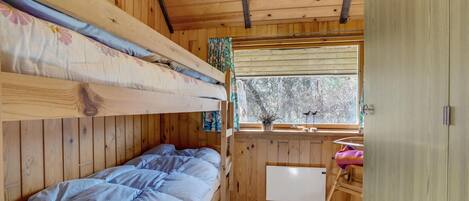 A cozy cabin room with a bunk bed, a small desk, and a window with a view of trees.