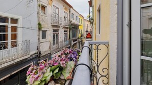 En smal gade med bygninger langs begge sider, en balkon med blomster og et skilt med 'DELTA'.