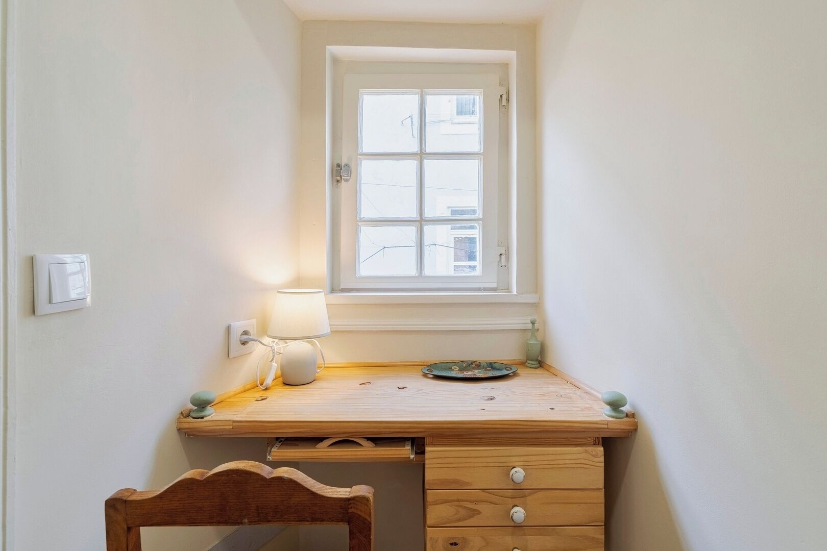 A small, tidy room with a wooden desk, a lamp, a window, and a chair.