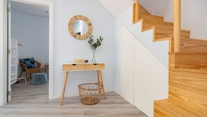 Ein modernes Interieur mit einer Holztreppe, einem runden Spiegel, einem kleinen Holztisch und Körben aus Weidengeflecht.