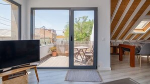 Eine moderne Wohnung mit einer großen Glasschiebetür, die auf einen Balkon führt, einem Flachbildfernseher auf einem Holzboden und einem Essbereich mit Tisch und Stühlen.