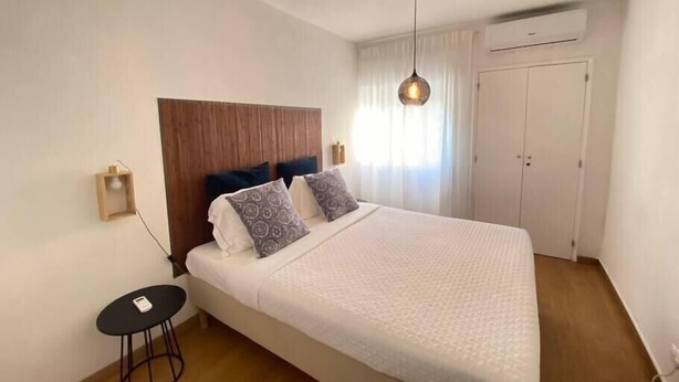 Une chambre avec une tête de lit en bois, un lit agrémenté d’oreillers à motifs, une petite table ronde et un luminaire suspendu.