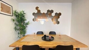 Un coin repas avec une table en bois, des chaises noires, un élément de décoration murale en forme d’hexagone et une plante en pot.