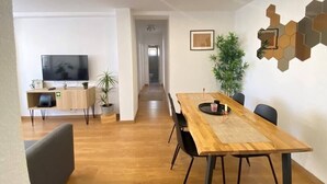 Un espace repas moderne avec une table en bois, des chaises noires et un téléviseur en arrière-plan.