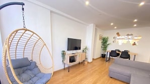 Un salon moderne avec un fauteuil suspendu, un canapé gris, un téléviseur, un coin repas et un plancher en bois.