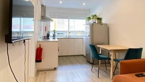 A modern kitchen with white cabinets, a stainless steel range hood, and a window above the sink. There is a small dining area with a table and two chairs. - Project Montalvão, Setúbal (Setúbal)