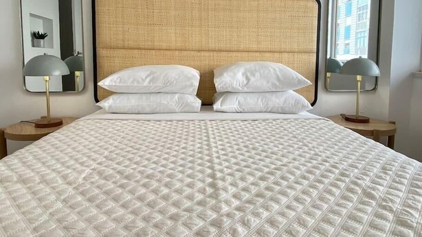 A neatly made bed with a quilted white duvet, two white pillows, and a wooden headboard. There are two bedside tables with lamps on either side of the bed. - Project Montalvão, Setúbal (Setúbal)