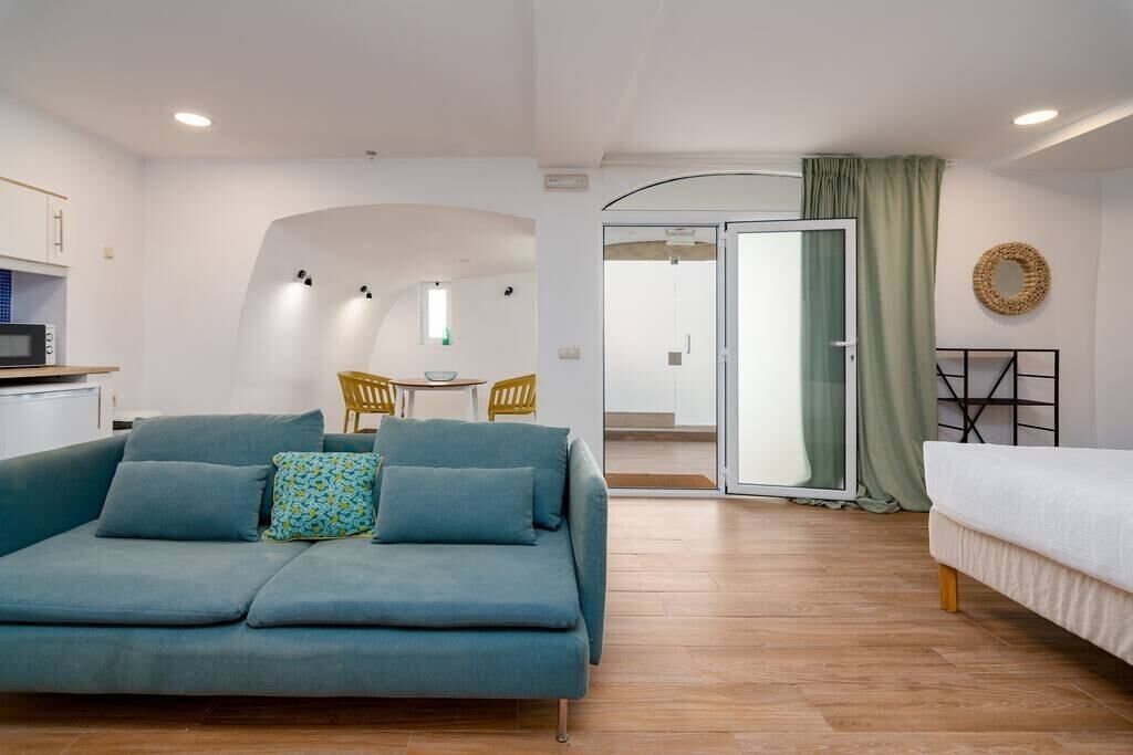 Ein moderner, gut beleuchteter Raum mit einer Couch, einem Bett, einem Essbereich und einer Küchenzeile.