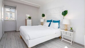 Une chambre moderne avec un grand lit, des murs blancs et une fenêtre.
