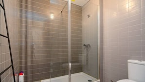 Een badkamer met een douche met glazen wand, een wit toilet en betegelde muren.