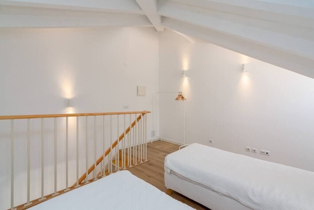 A bedroom with a wooden staircase, white walls, and a single bed.