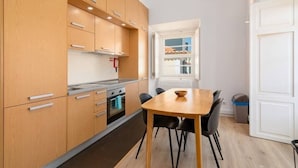 Een kleine keuken met houten kastjes, een fornuis en een eettafel met stoelen.