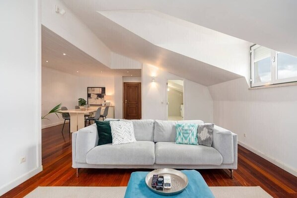 A modern living room with a grey sofa, a coffee table, and a dining area in the background.