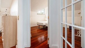 Ein Zimmer mit Holzboden, einem Bett, einem Nachttisch und einem Fenster.