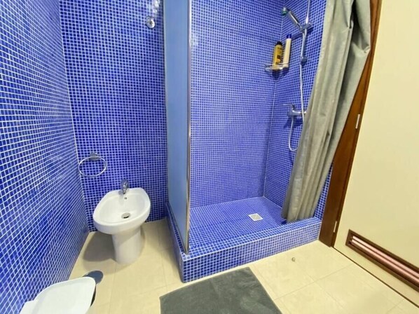 Une salle de bain avec des murs recouverts de carreaux bleus, un lavabo blanc et un espace douche.