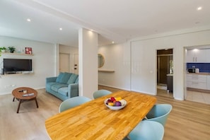 A modern living room with a wooden dining table, light blue chairs, a sofa, and a TV. - Zenith Setúbal (Setúbal)