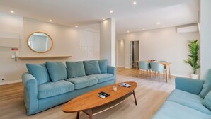 Een moderne woonkamer met een blauwe bank, een houten salontafel en een eethoek met een tafel en stoelen.