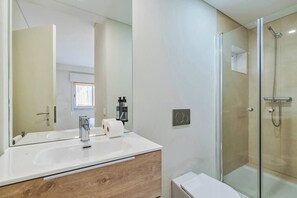 Een moderne badkamer met een douchecabine van glas, een wit wastafelmeubel met houten details en een grote spiegel.