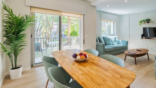 Een moderne woonkamer met een houten eettafel, groene stoelen, een bank en een televisie.