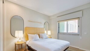 Een slaapkamer met een bed, twee nachtkastjes met lampen, een grote spiegel en een raam.