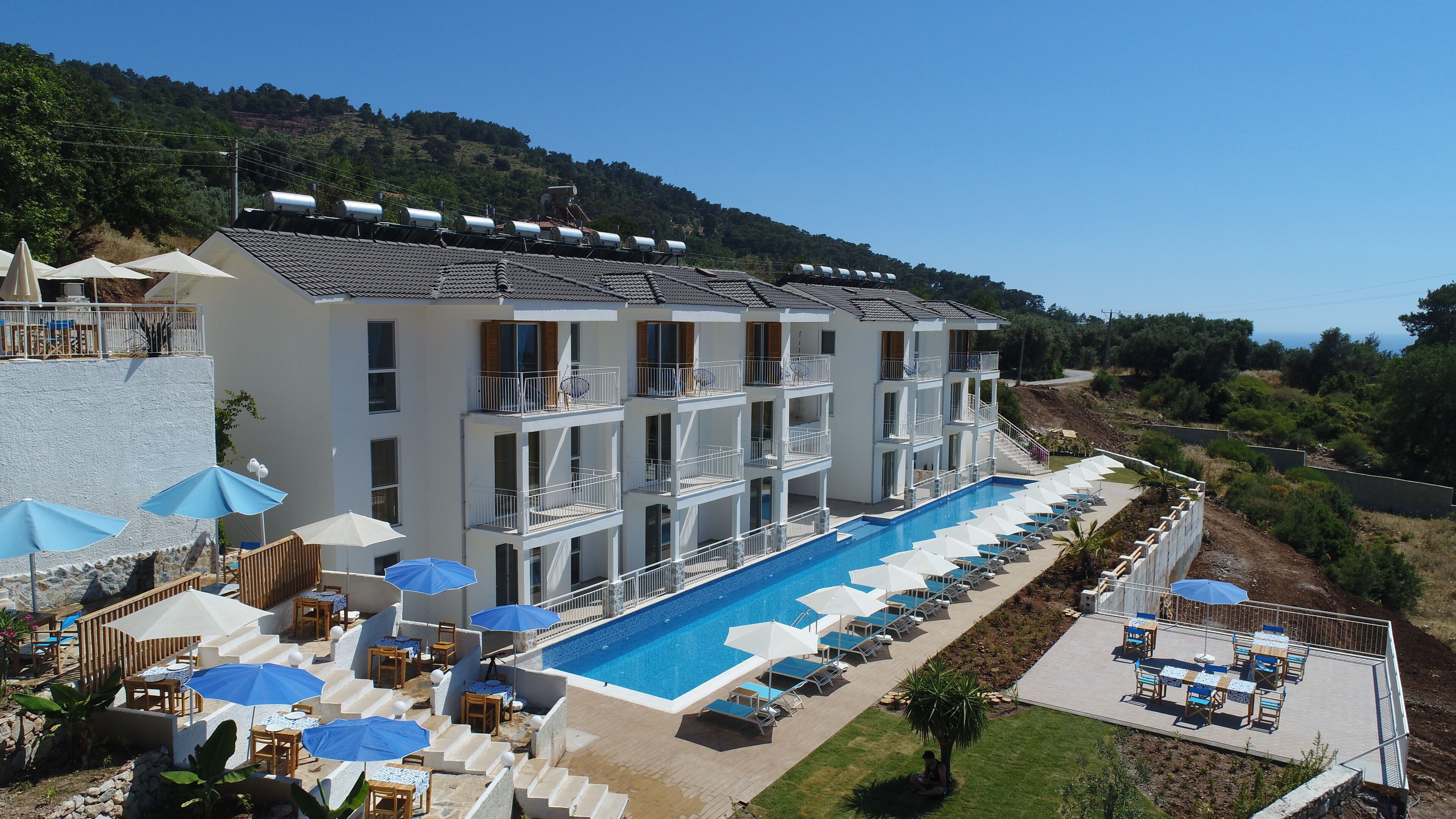 A multi-story hotel with a swimming pool, outdoor seating, and a view of the surrounding landscape.