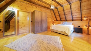 Une chambre confortable, aménagée dans un chalet en bois, avec un lit, une table de chevet, une armoire et un escalier menant à un étage supérieur.