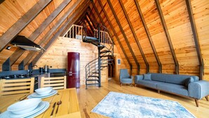 Une pièce confortable aménagée comme un grenier, avec un intérieur en bois, un coin repas comprenant une table et des chaises, un canapé et un escalier en colimaçon menant à un niveau supérieur.