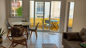 A spacious living area with a dining table, chairs, a sofa, and a large window offering a view of the outside.