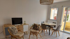 A modern living room with a TV, dining table, wicker chairs, and a sofa.