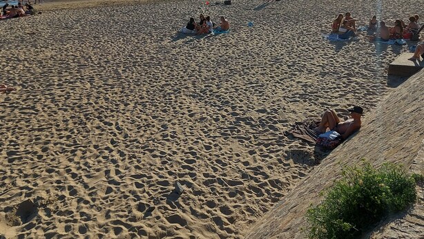 A crowded beach with people sunbathing and walking along the shore.