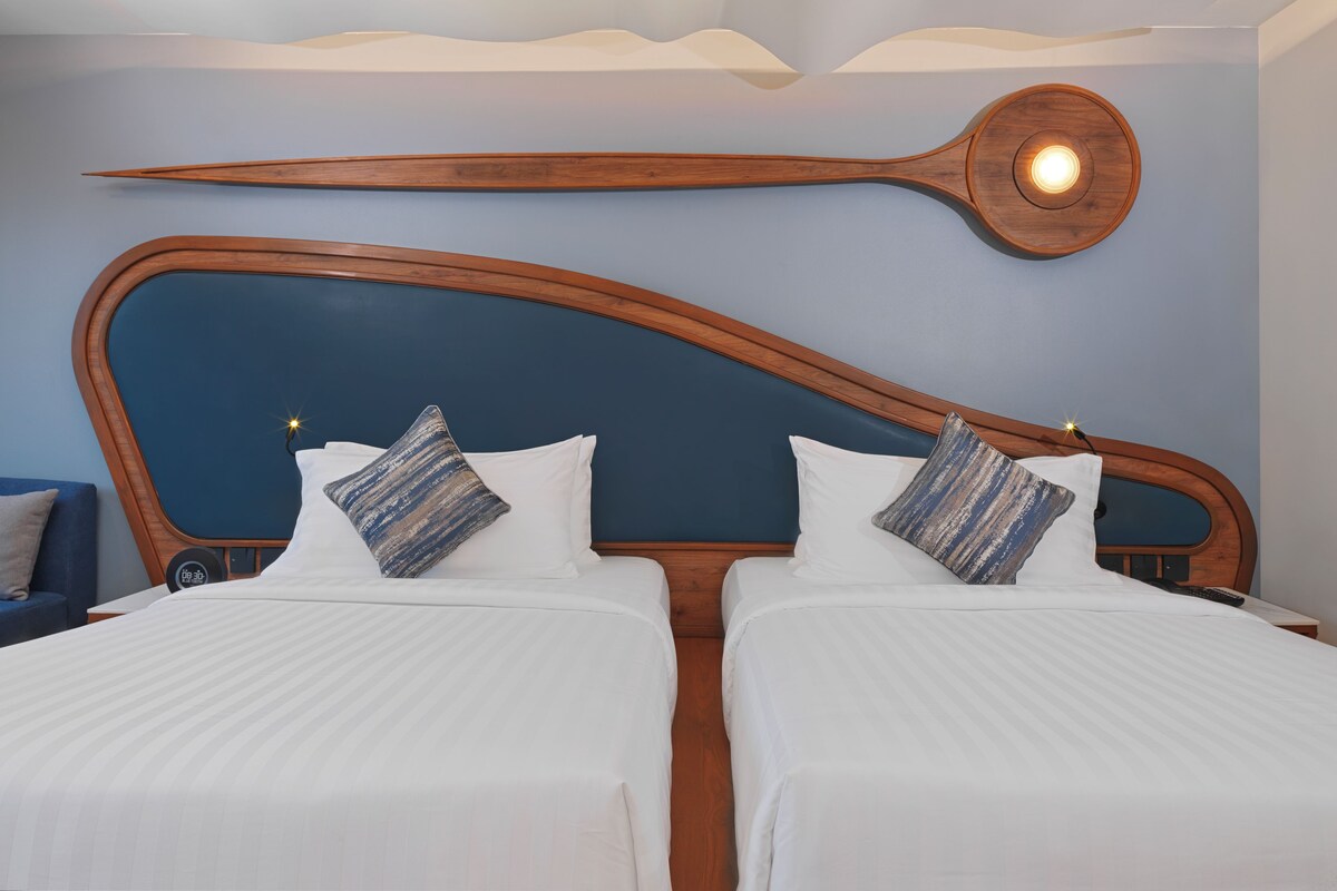 A hotel room with a modern design, featuring a large wooden headboard, two beds with white linens, and a unique wall-mounted light fixture.