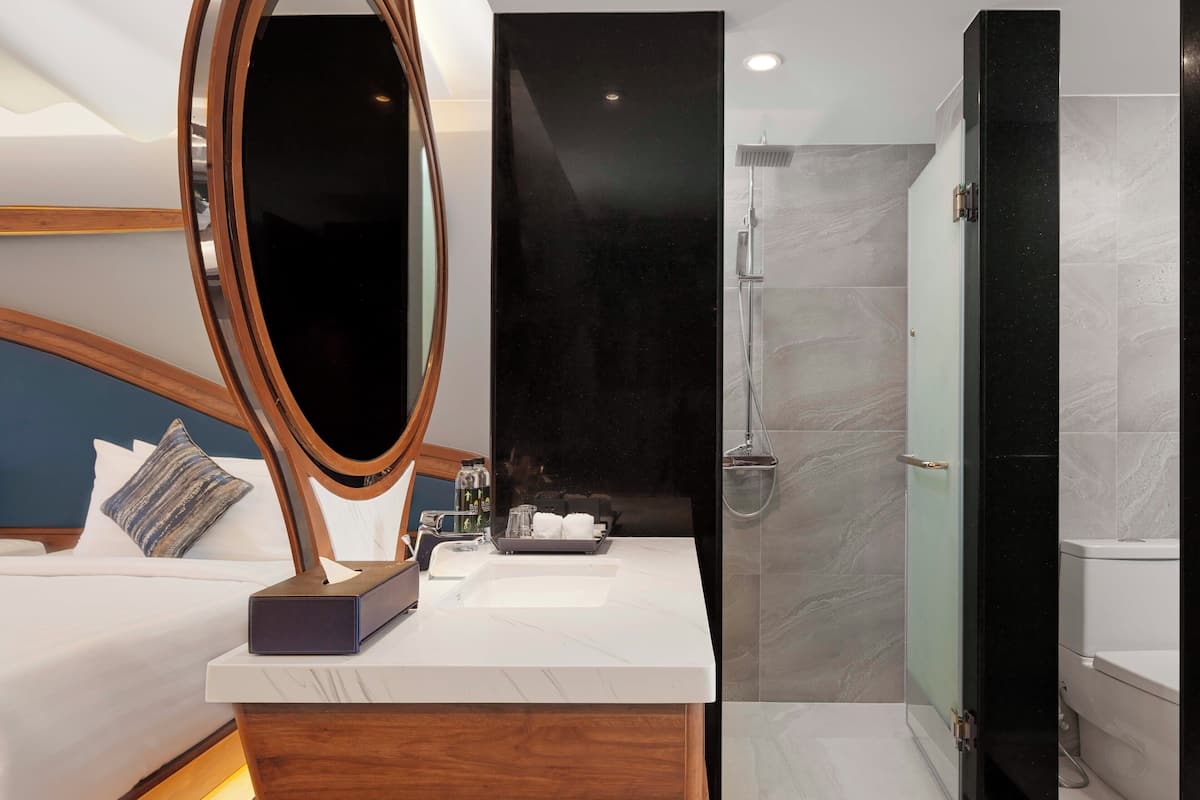 A modern bathroom with a large mirror, a shower, and a bedside table with toiletries.
