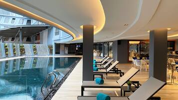 A modern indoor pool area with lounge chairs and a waterfall feature.