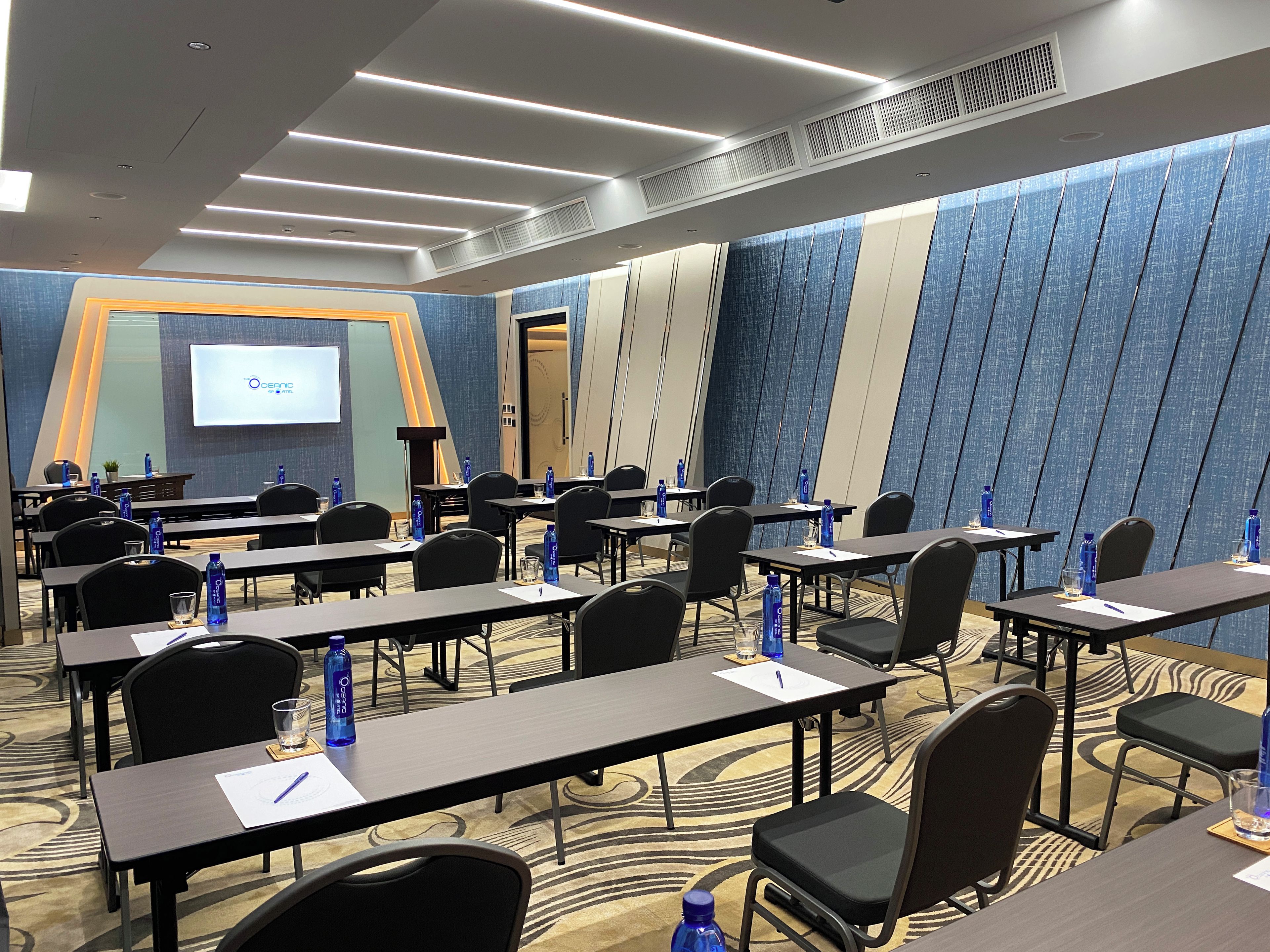A conference room with tables, chairs, and a presentation screen.