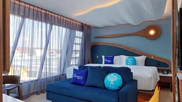 A hotel room with a bed, a blue sofa, a wooden headboard, and a view of the outside.