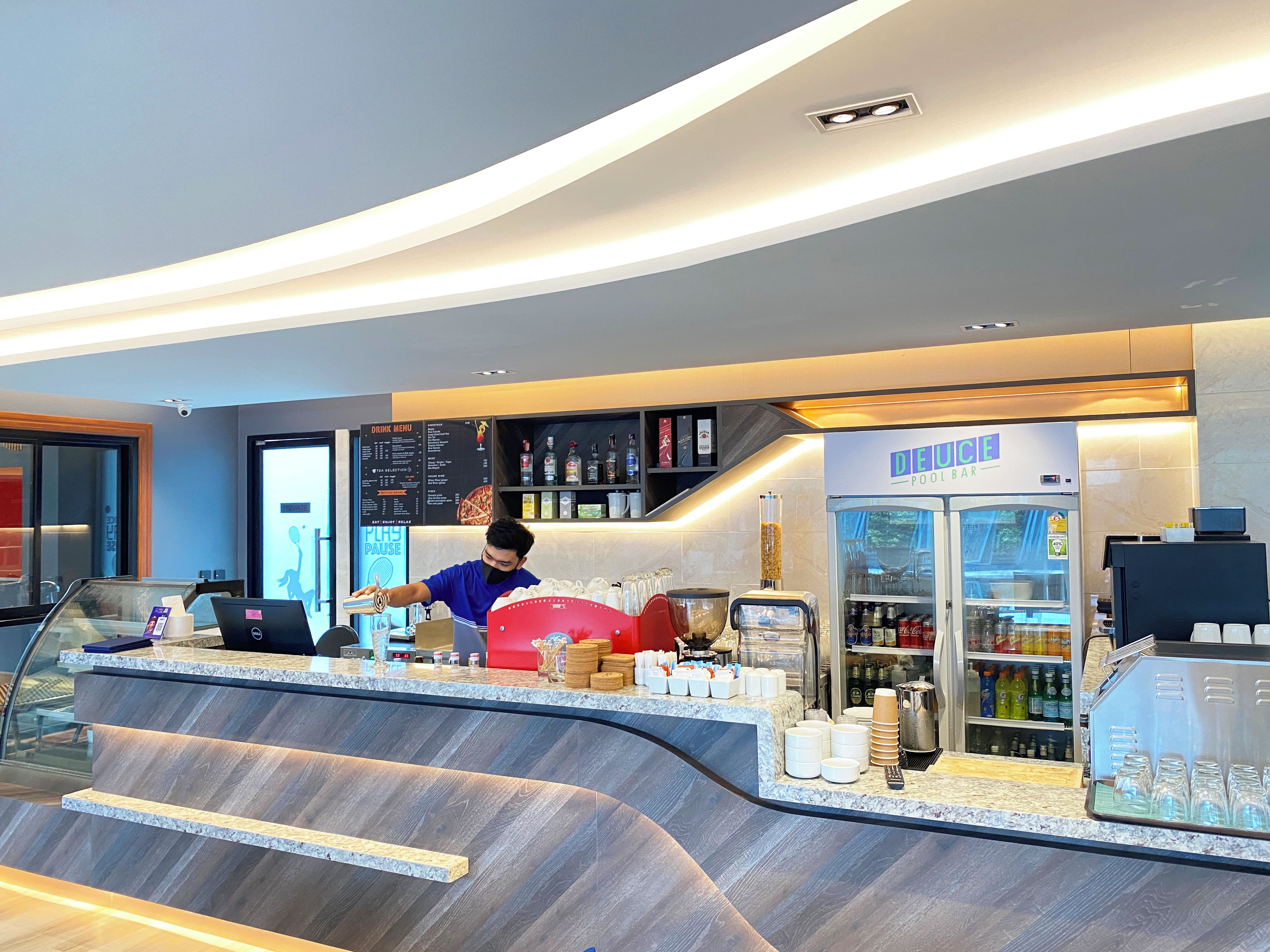 A modern bar area with a counter, a beverage dispenser, and a refrigerated display.