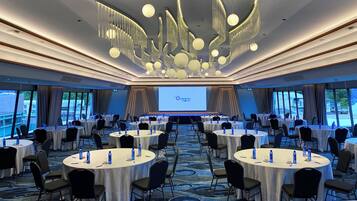 A conference room with multiple round tables, chairs, and a large screen displaying 'Oceanic Hotel'.