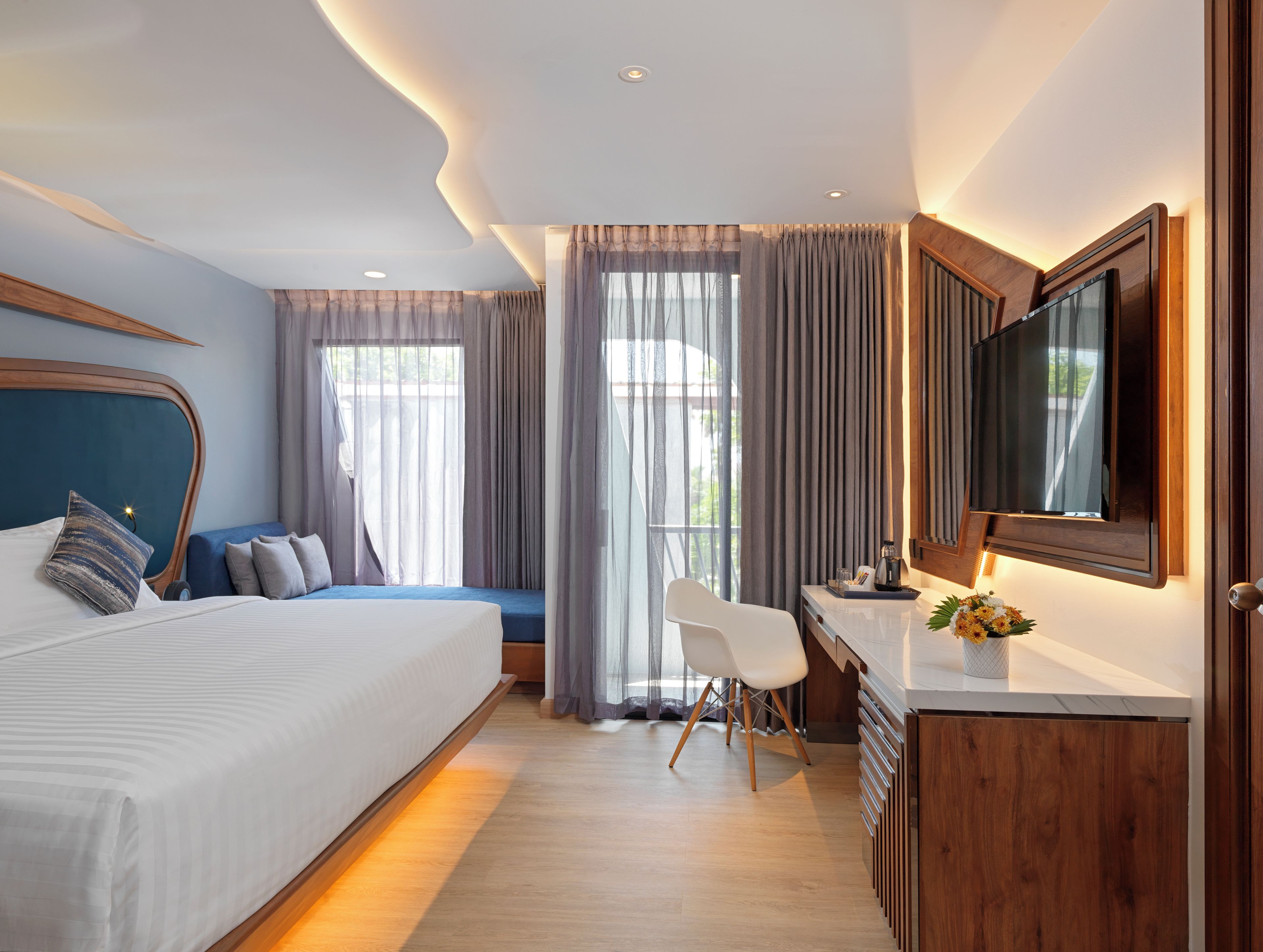 Una habitación de hotel moderna con una cama grande, un escritorio, una silla, un televisor y vistas al exterior.