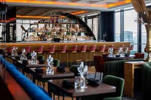 A bar area with a variety of bottles and glasses, seating with tables, and a view through large windows. - The Oceanic Sportel (Ko Kaeo)