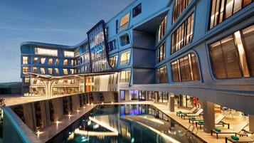 A modern hotel with a pool, multiple balconies, and a rooftop terrace.