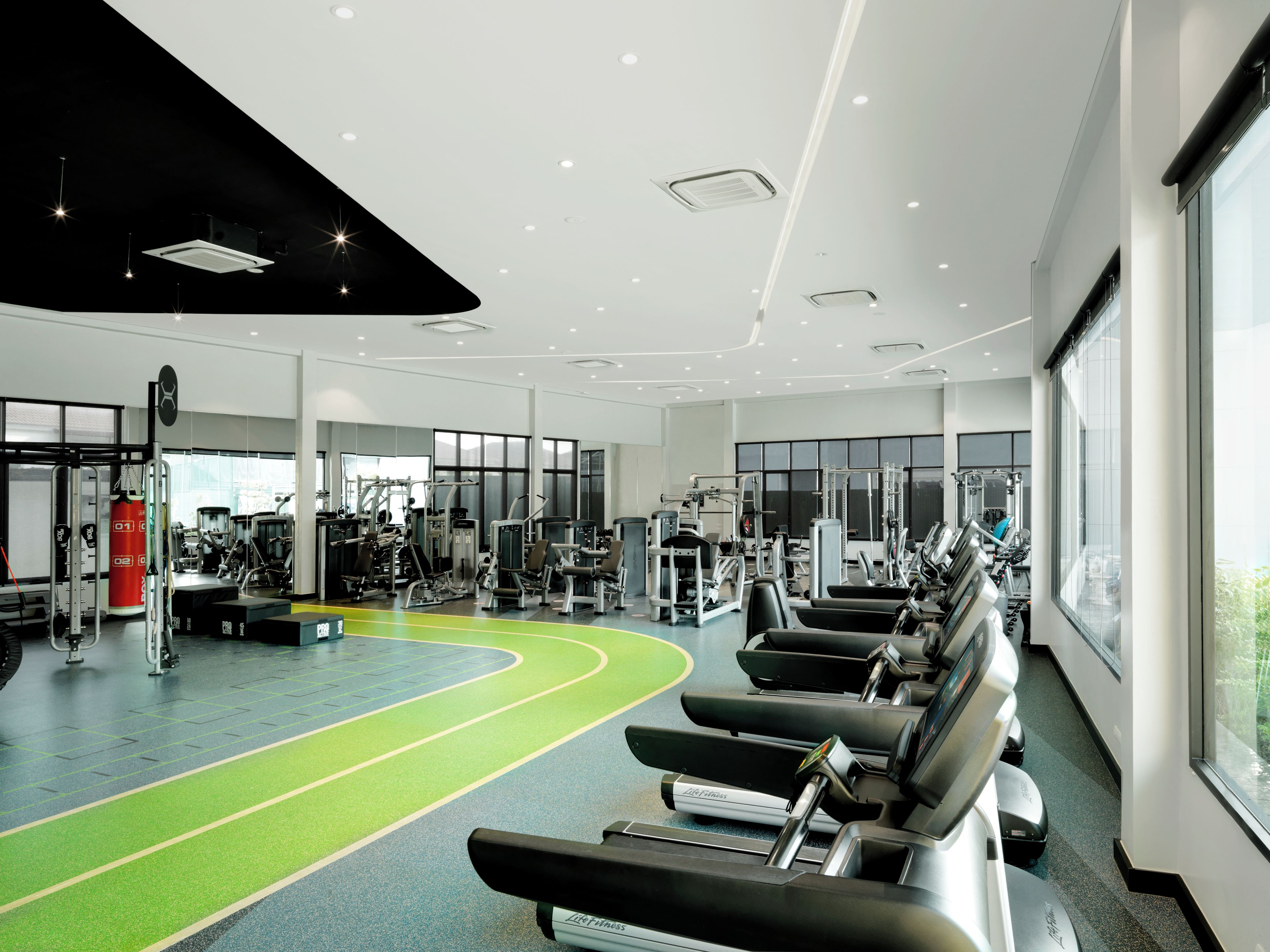 A modern gym with treadmills, weight machines, and a green running track.