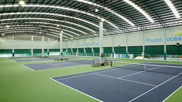 Pista de tenis interior con varias canchas, techo alto con vigas metálicas y una amplia pared verde con señalización.