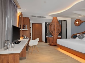 A modern hotel room with a wooden desk, a flat-screen TV, a bed, and a unique decorative wall piece. - The Oceanic Sportel (Ko Kaeo)