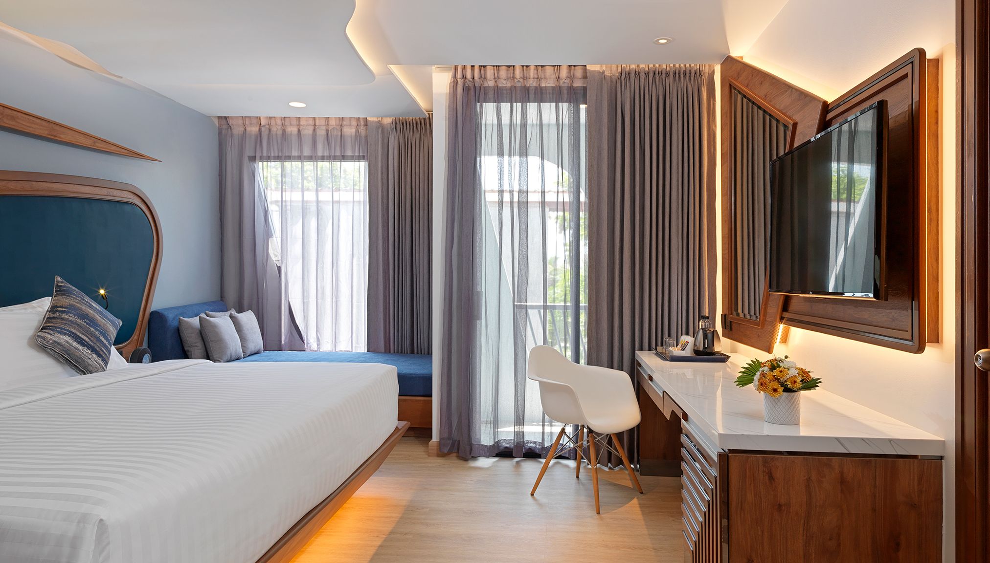 Una habitación de hotel con cama, escritorio, silla, televisor y cortinas.