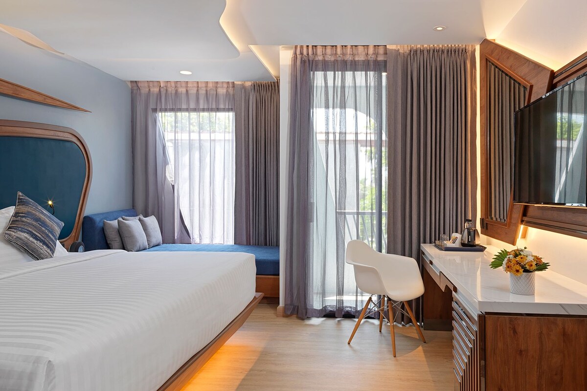 A hotel room with a bed, a desk, a chair, a TV, and curtains.