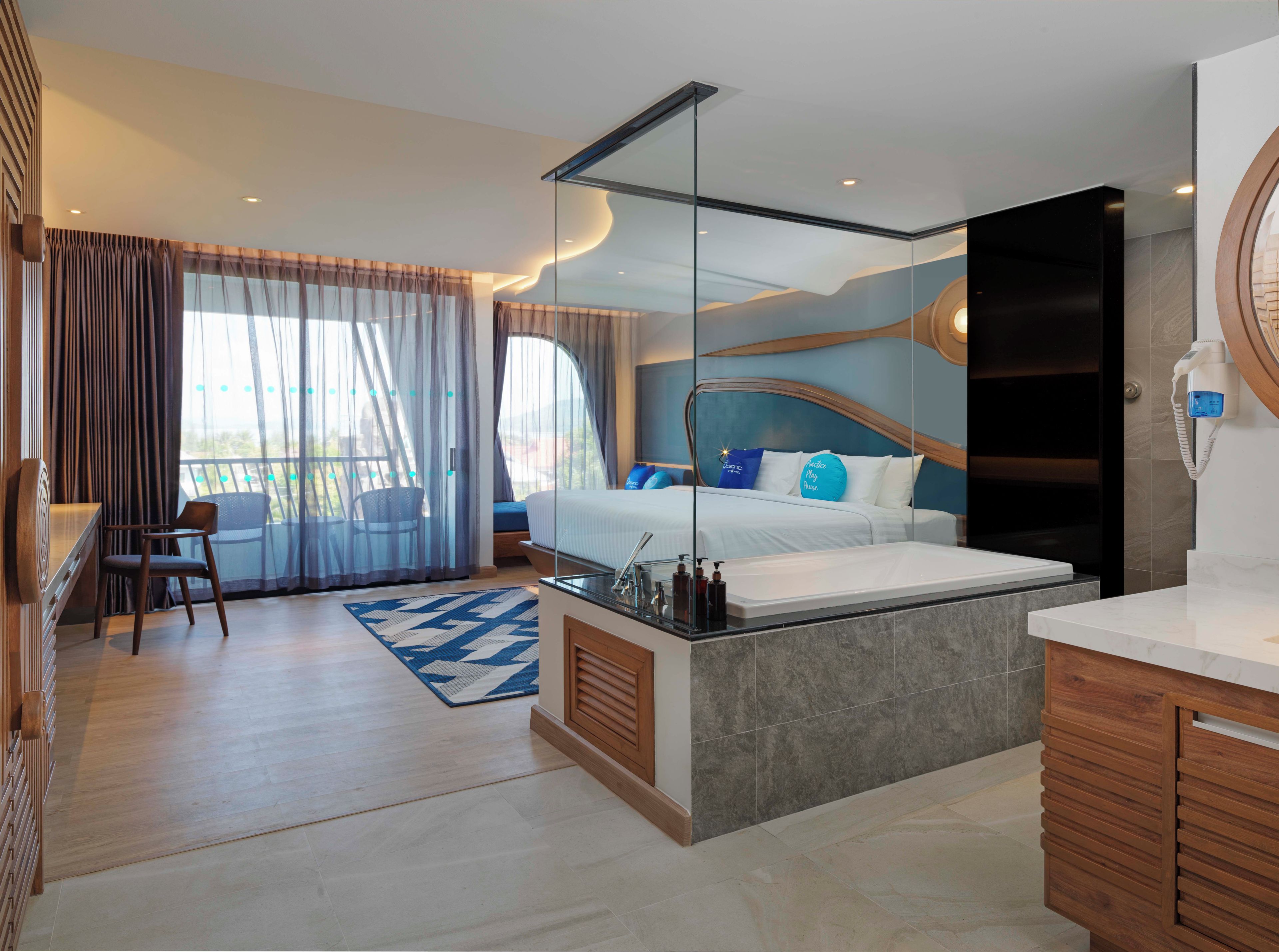 A modern hotel room with a large bed, a sitting area with a chair, a small desk, and a bathroom with a mirror and sink.