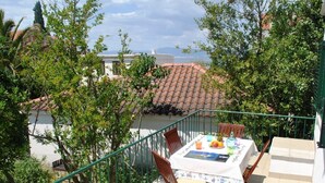 A balcony with a table set for two, surrounded by greenery and overlooking a tiled roof. - Nice 2-bedroom Private House, 50 m Beach, Sutivan (Sutivan)