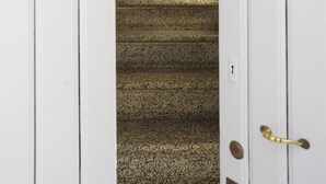 Una escalera con alfombra texturizada que conduce a un rellano con un adorno en la pared.